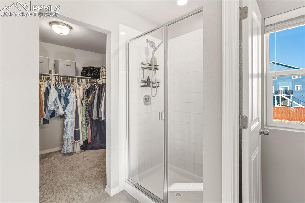 Full bath featuring a walk in closet, light colored carpet, a shower stall, and light tile patterned floors