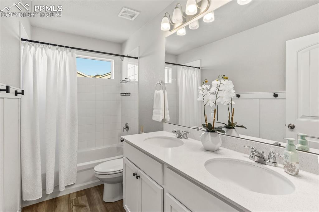 Full bathroom with double vanity, shower / bath combo, and dark wood-style flooring