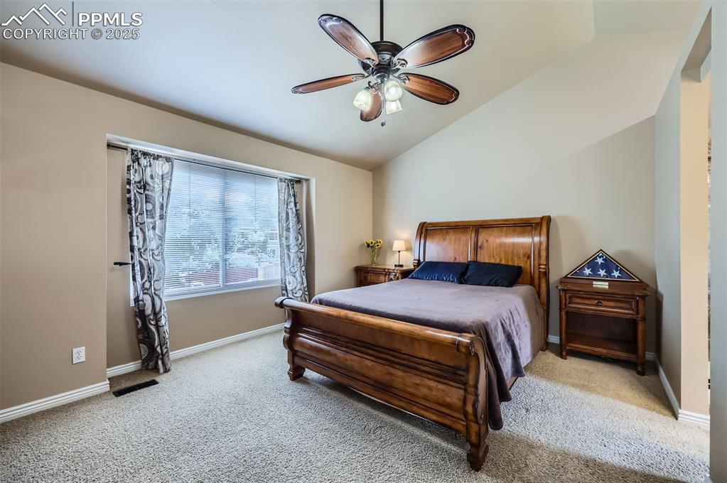 Bedroom featuring light carpet, vaulted ceiling, and a ceiling fan