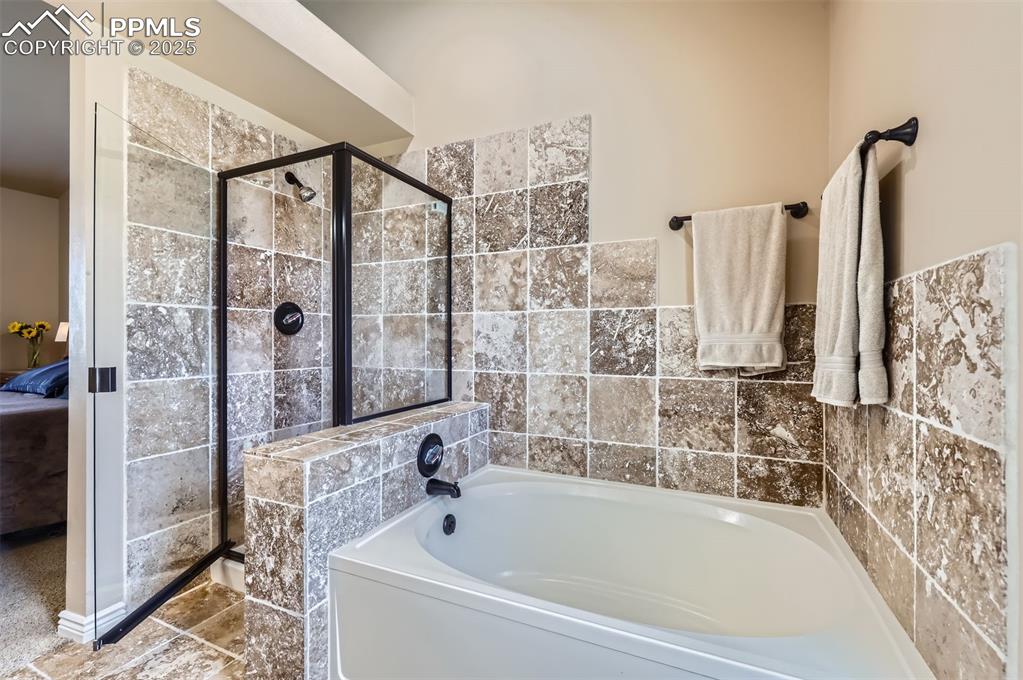 Ensuite master bathroom featuring a bath, a shower stall, and Travertine tile walls