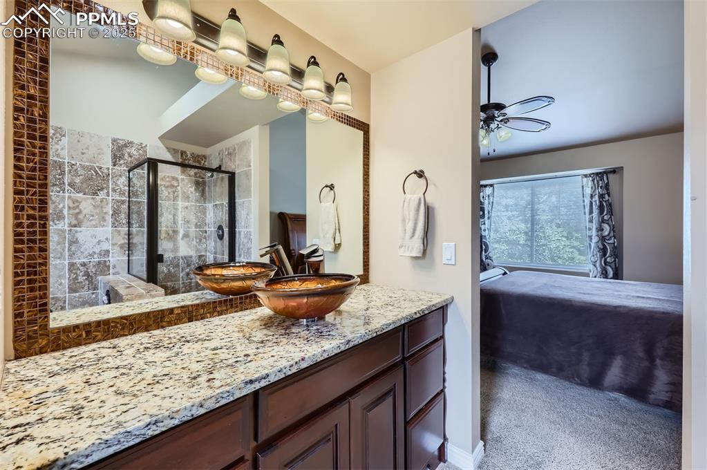 Ensuite bathroom with vanity, a ceiling fan, and a Travertine tile shower