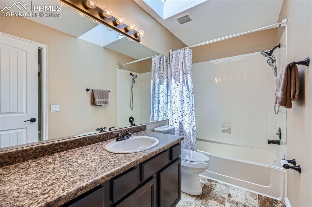 Full Jack and Jill bath featuring vanity, shower / bathtub combination with curtain, and a skylight