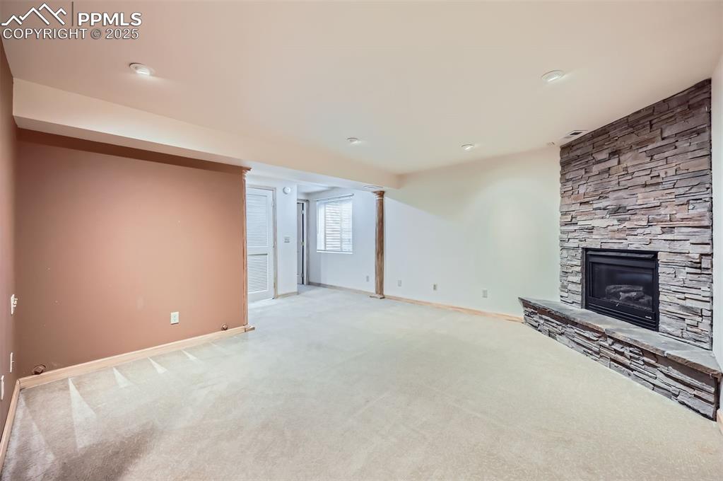 Unfurnished family room with a stone fireplace, light colored carpet, and ornate columns