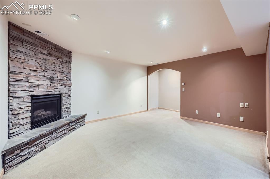 Unfurnished family room with a stone fireplace, arched walkways, light colored carpet, and recessed lighting