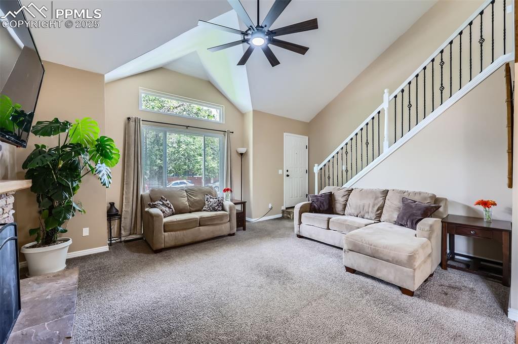 Carpeted living area featuring stairway, a ceiling fan, and vaulted ceiling