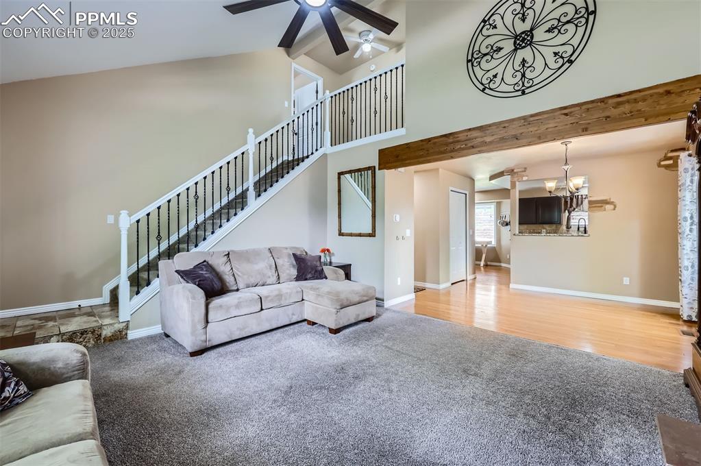 Living room featuring carpet and wood flooring, a ceiling fan, beamed ceiling, high vaulted ceiling, and stairs