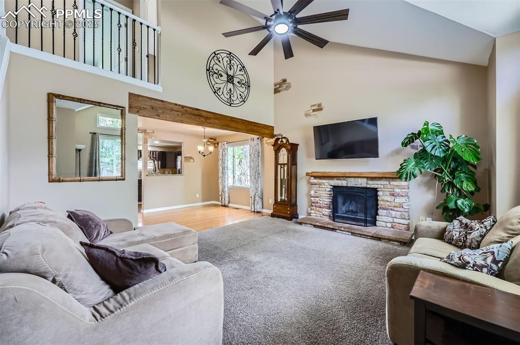 Living area featuring a ceiling fan, a chandelier, a stone fireplace, high vaulted ceiling, and wood finished floors