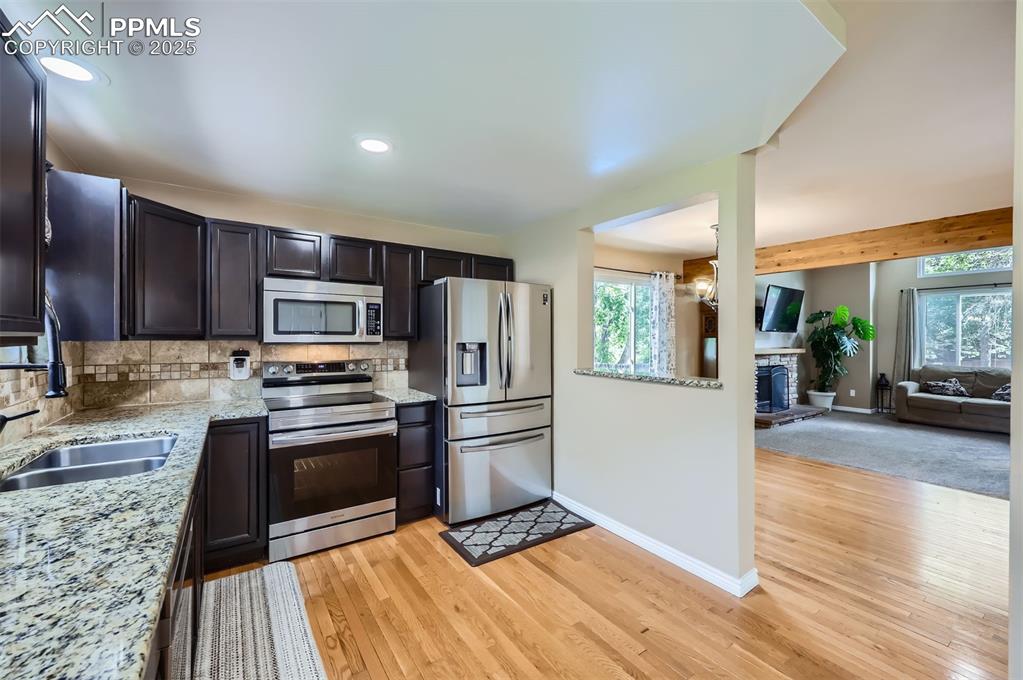 Kitchen featuring some stainless steel smart appliances, backsplash, light granite countertops, light wood floors, and recessed lighting