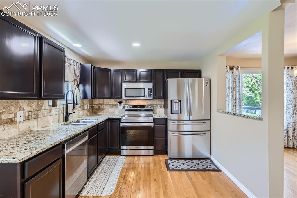 Kitchen featuring appliances with stainless steel finishes, decorative backsplash, light wood floors, light granite counters, and recessed lighting