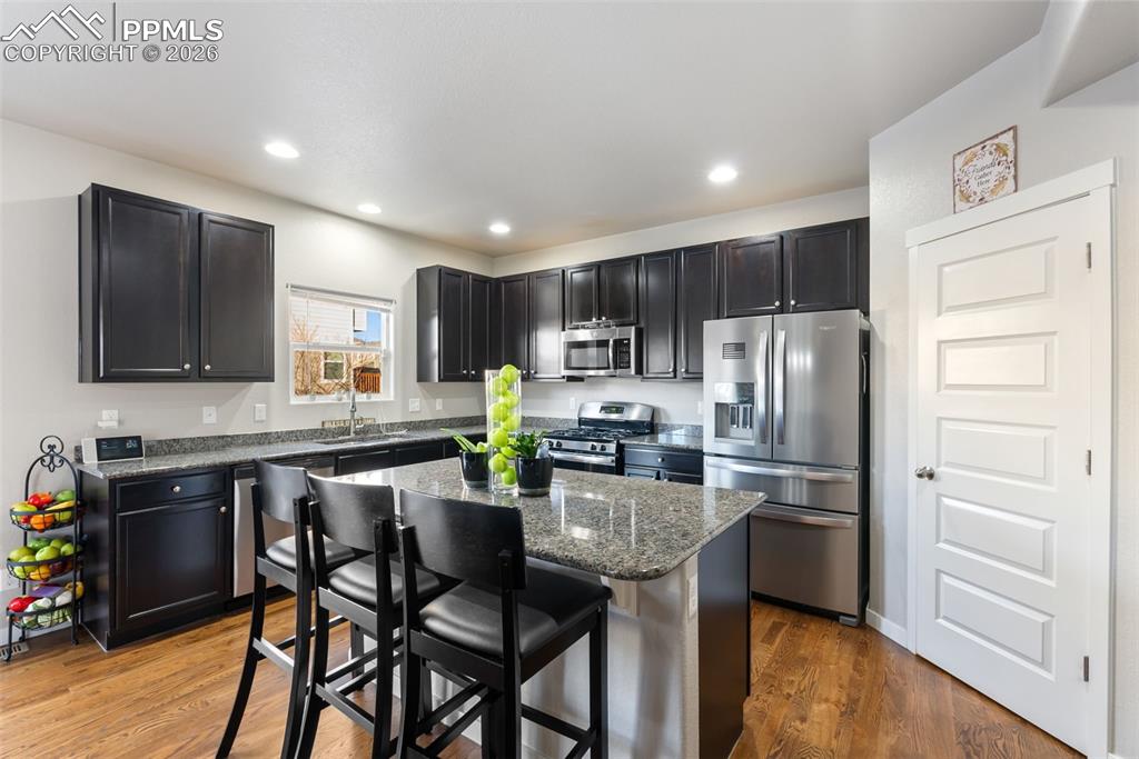 Modern kitchen with oversized granite island, stainless steel appliances, gas range, and recessed lighting.