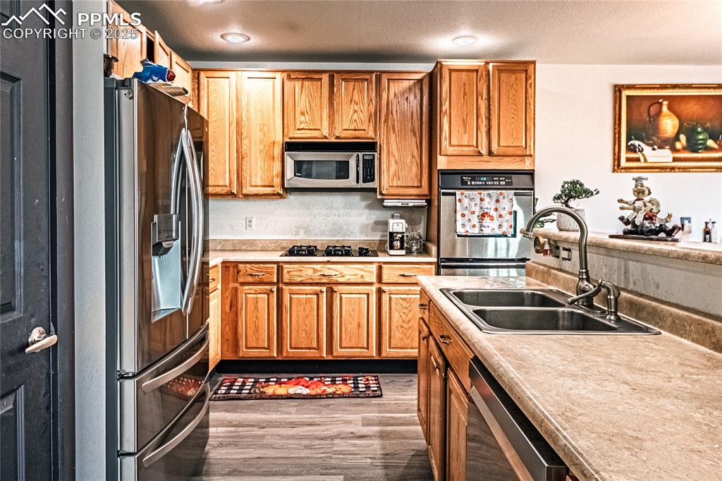 Kitchen with light countertops, stainless steel appliances, light wood-style floors, brown cabinetry, and a textured ceiling