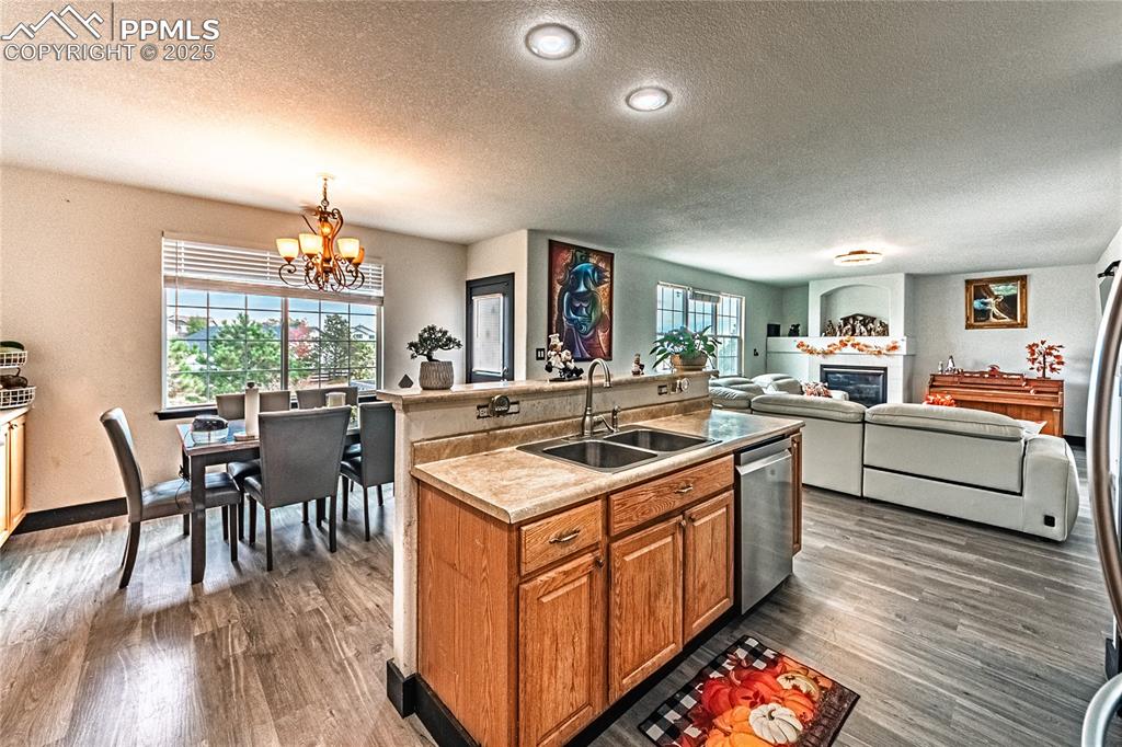 Kitchen with brown cabinets, a textured ceiling, a kitchen island with sink, a chandelier, and light countertops