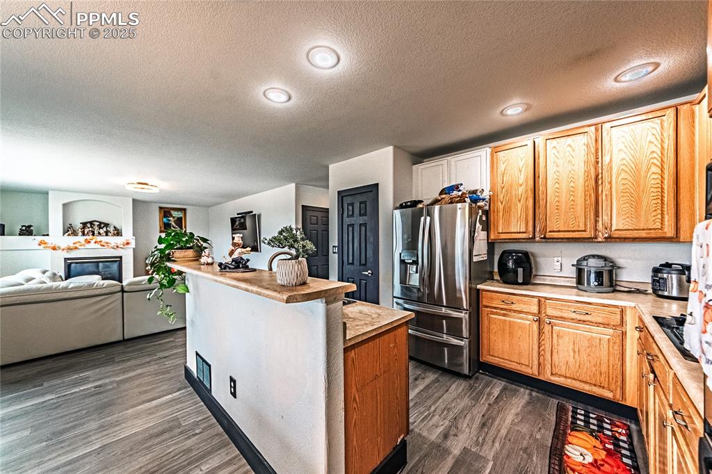 Kitchen with a textured ceiling, stainless steel refrigerator with ice dispenser, a glass covered fireplace, light countertops, and a center island