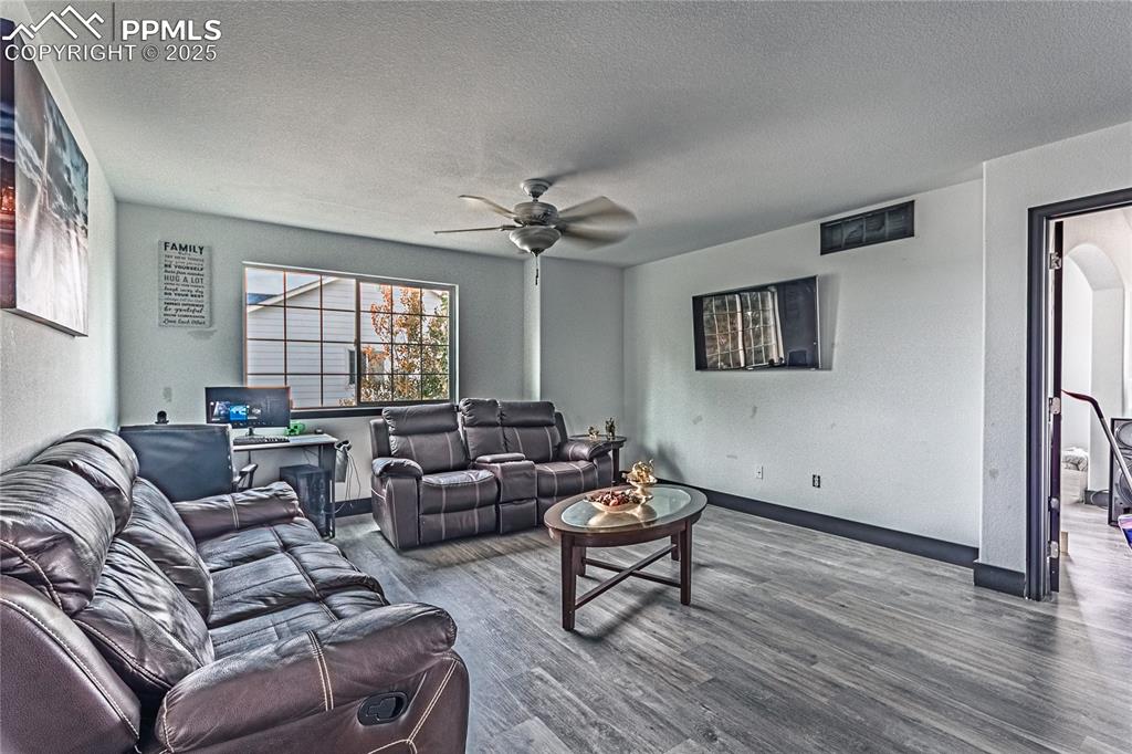 Living area with wood finished floors, a textured ceiling, a ceiling fan, and a textured wall