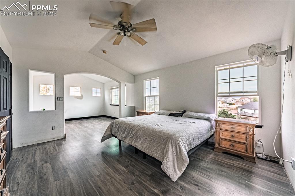 Bedroom with dark wood finished floors, lofted ceiling, a ceiling fan, and arched walkways