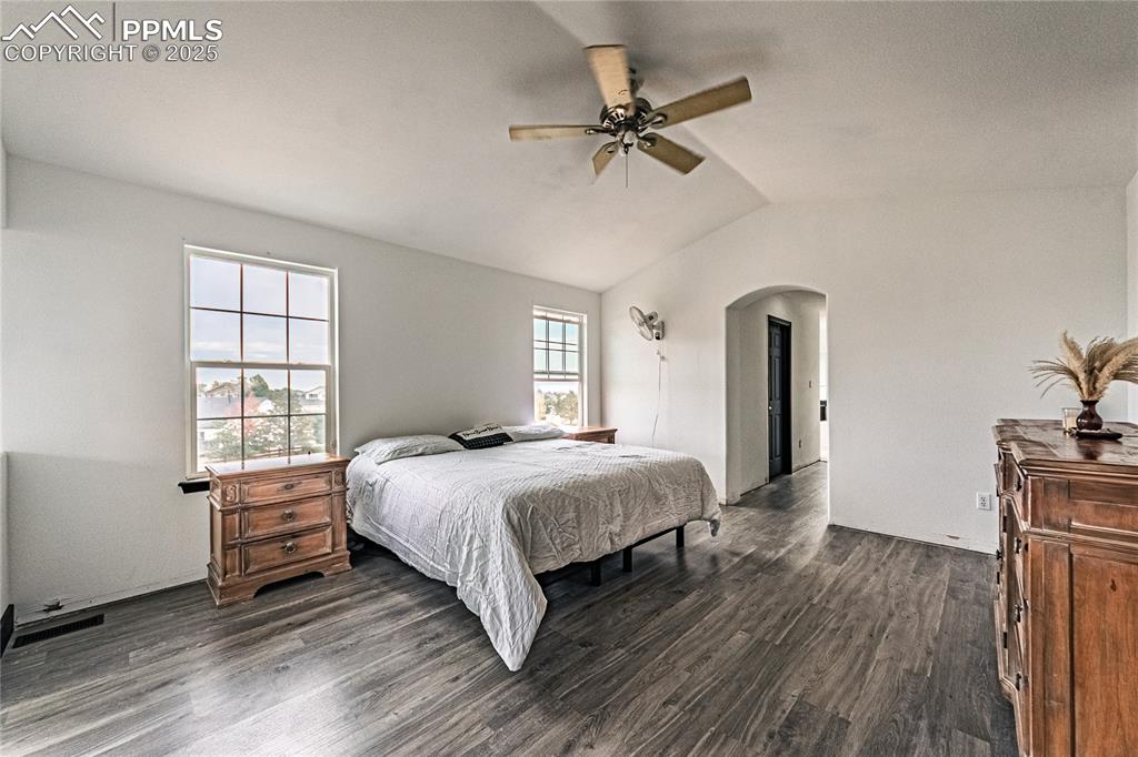Bedroom featuring dark wood-style flooring, vaulted ceiling, ceiling fan, and arched walkways