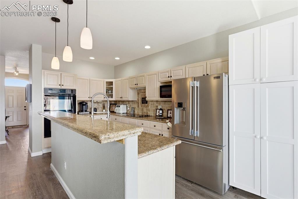 Kitchen with stone pendant lighting, a kitchen island with sink, light stone counters, and grey floors