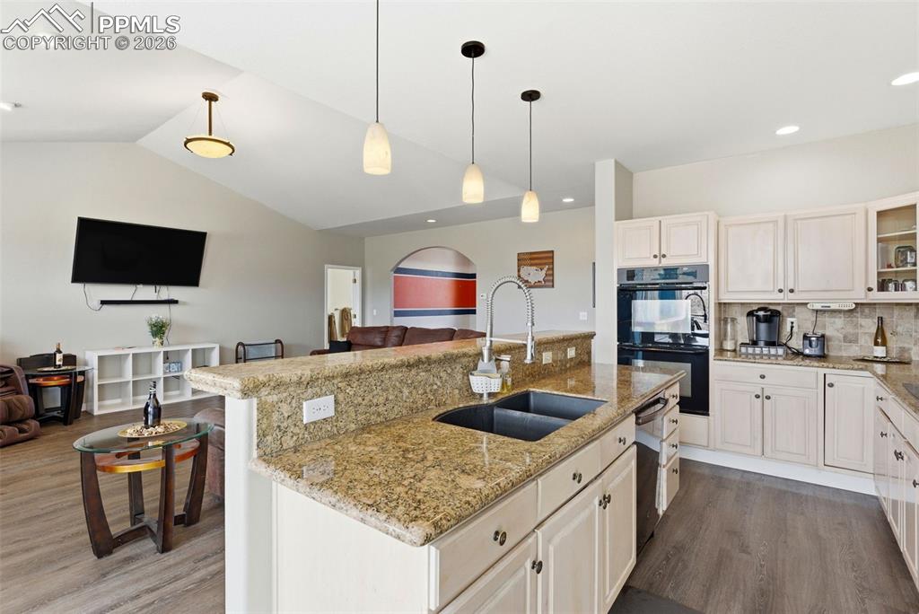 Kitchen with lots of cabinets, a center island with sink, light wood-style floors, light stone counters, and hanging light fixtures