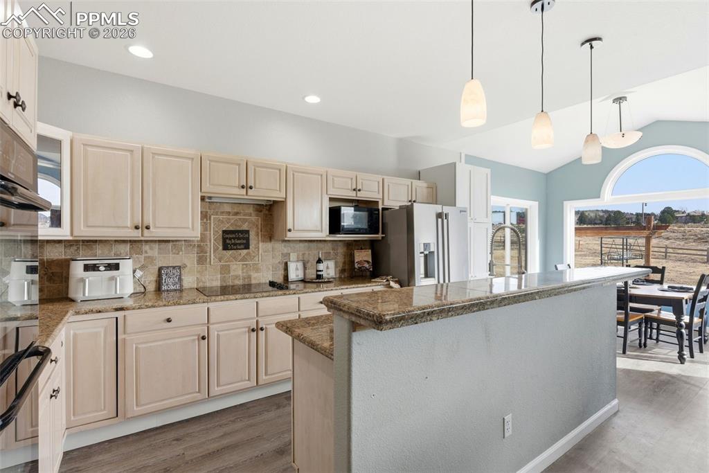 Kitchen with healthy amount of natural light, decorative light fixtures, light wood finished floors, lofted ceiling, and backsplash