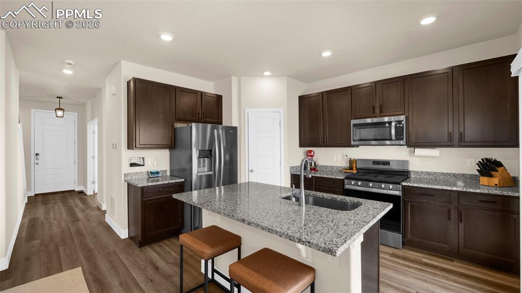 Kitchen with light stone countertops, a breakfast bar, stainless steel appliances, light wood-style floors, and dark wood finish cabinets