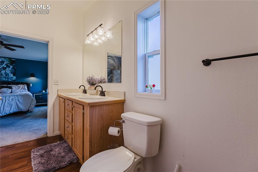 Ensuite bathroom featuring double vanity, ceiling fan, and dark wood-style floors