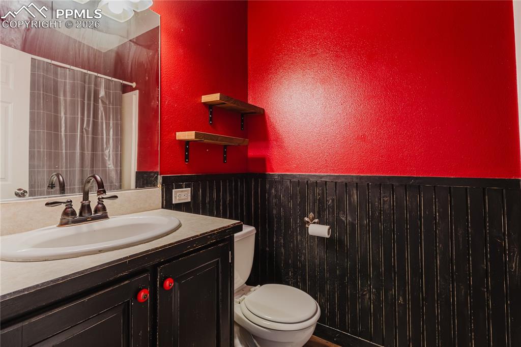 Full bathroom featuring a textured wall, vanity, a shower with curtain, and a wainscoted wall