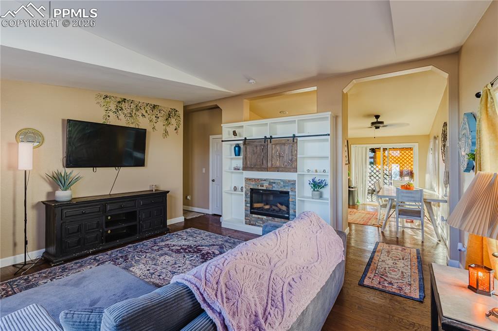 Living room with vaulted ceiling, a fireplace, dark wood-style floors, and a ceiling fan