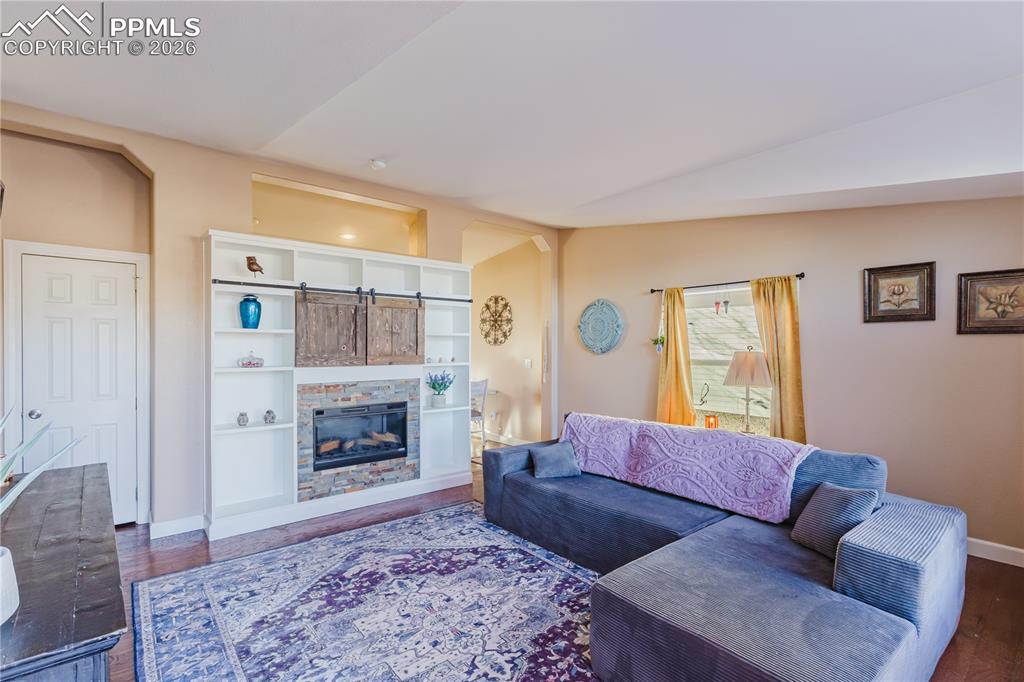 Living room featuring dark wood-type flooring, a glass covered fireplace, and lofted ceiling