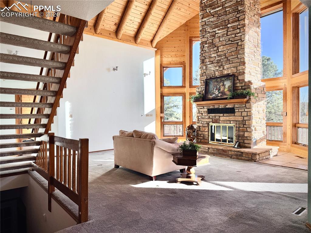 Living area with a high wooden beamed ceiling, carpet floors, a stone fireplace, and wooden walls