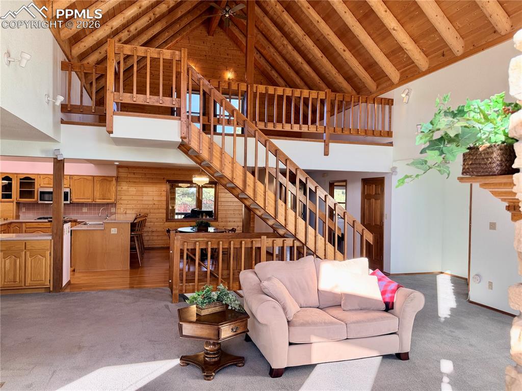 Carpeted living room featuring a high wood beamed ceiling and a ceiling fan