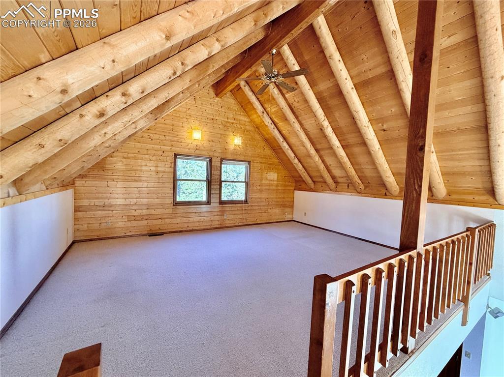 Additional living space with carpet flooring, a wood ceiling with exposed beams, and wooden walls