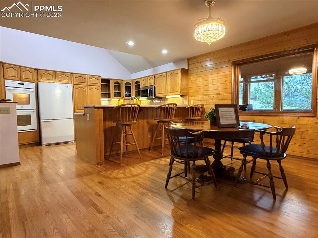Dining space with vaulted ceiling, recessed lighting, light wood finished floors, and wooden walls