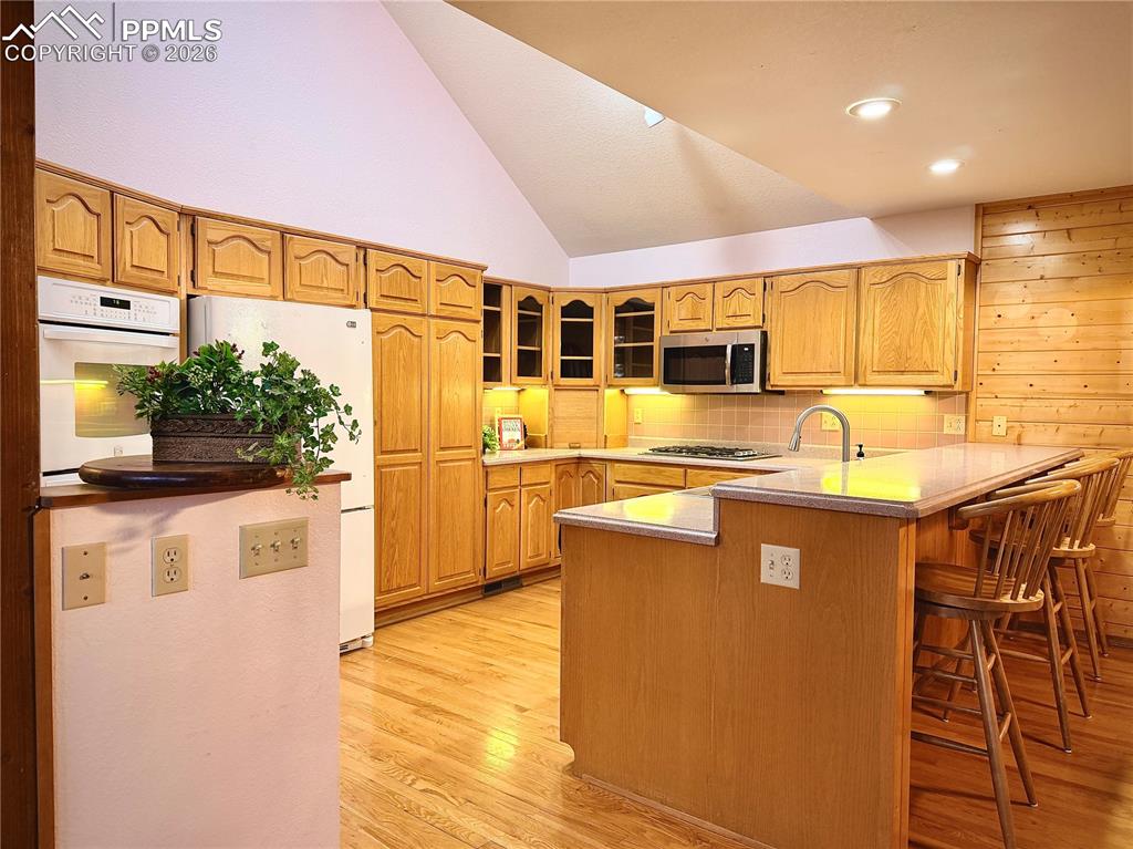 Kitchen with lofted ceiling, white appliances, glass insert cabinets, light countertops, and light wood-type flooring