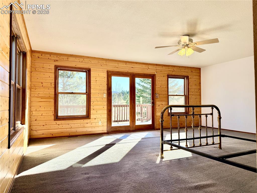 Bedroom with carpet, wood walls, access to outside, ceiling fan, and a textured ceiling