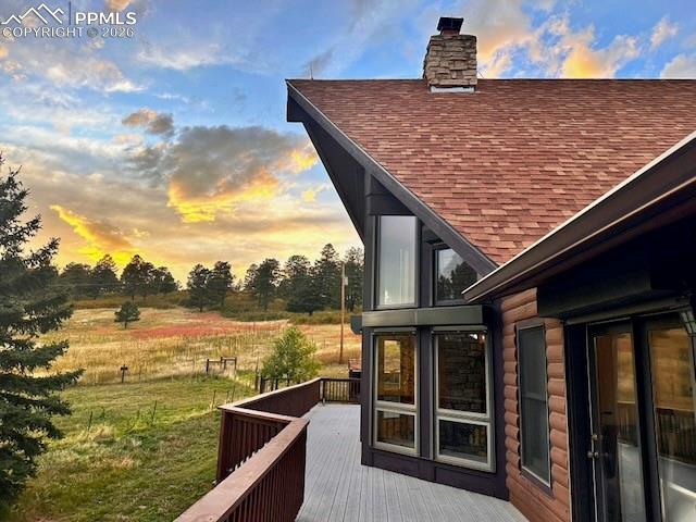 View of side of property with a shingled roof, a chimney, and a composite deck