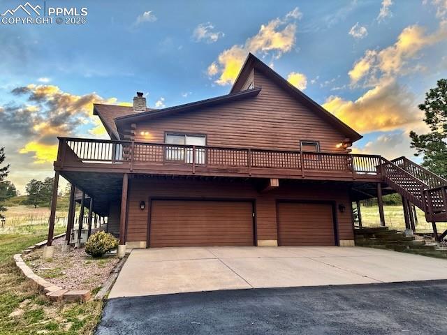 View of front facade with a deck, driveway, a chimney, and an attached garage