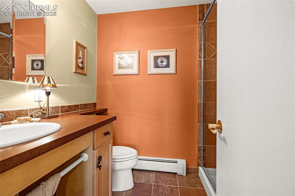 Full bathroom, basement featuring vanity, baseboard heating, a stall shower, and a textured wall