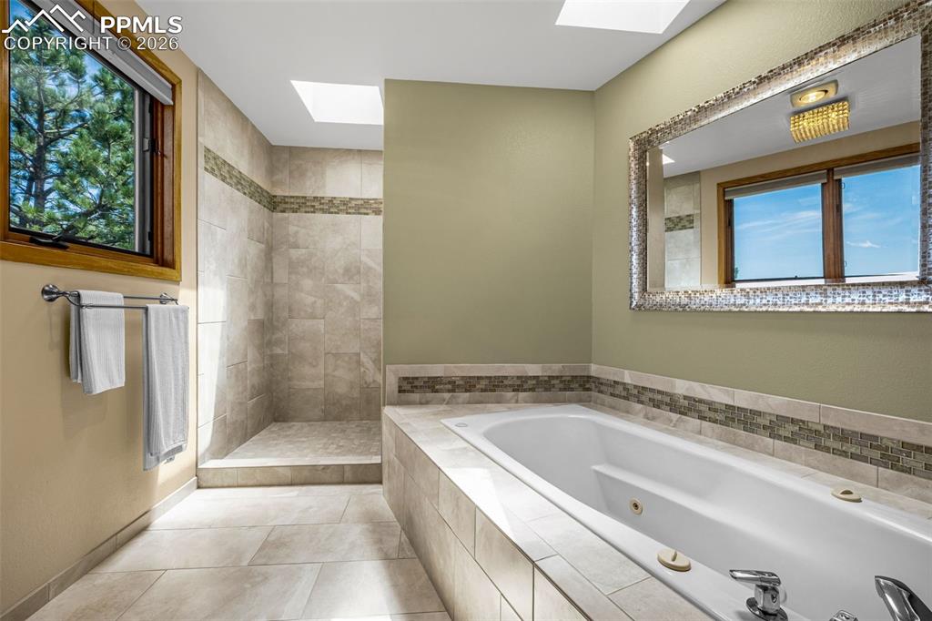 Full bath with a skylight, tiled shower, a jetted tub, and light tile patterned floors