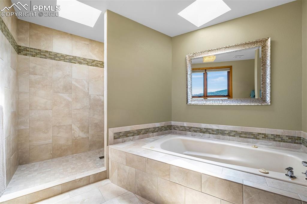 Bathroom featuring a skylight, tiled shower, light tile patterned floors, and a garden tub
