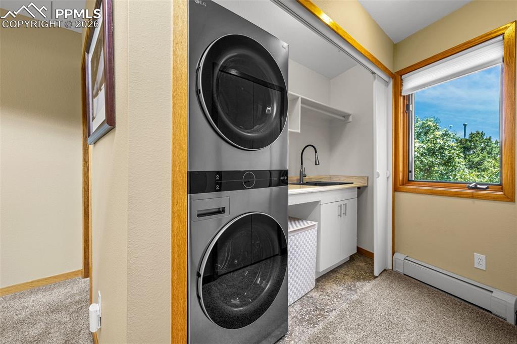 Laundry area with a baseboard heating unit, light carpet, and stacked washer / dryer