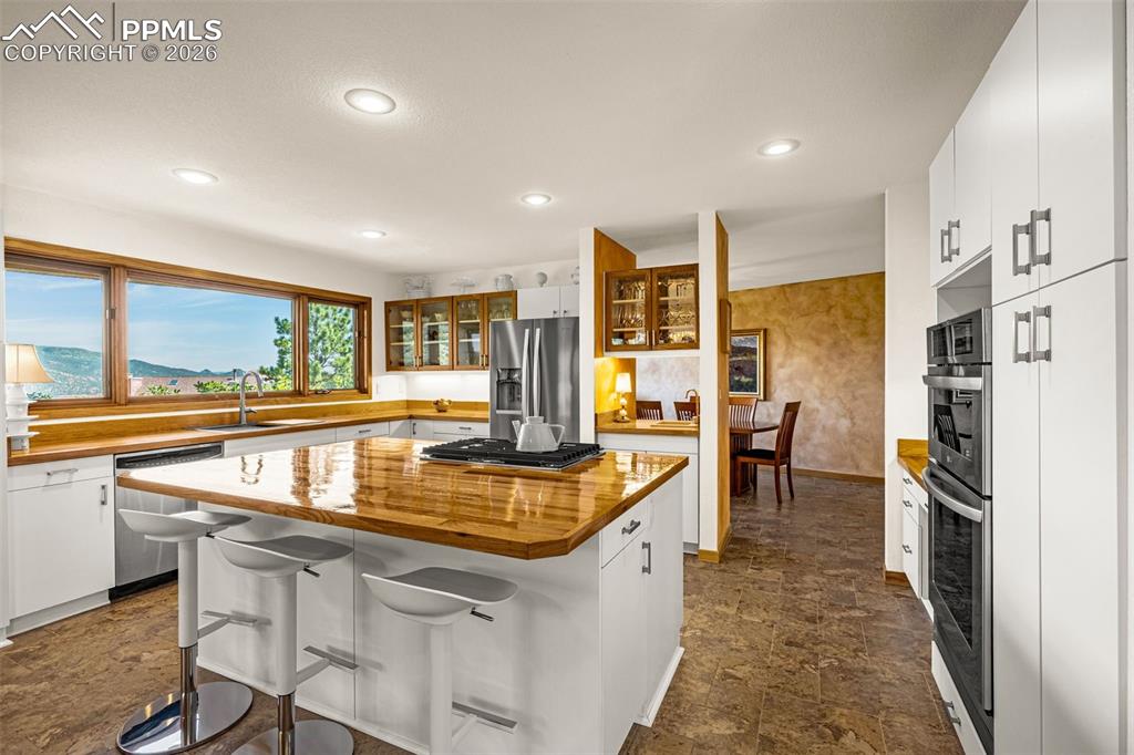 Kitchen featuring butcher block counters, white cabinets, stone finish flooring, a breakfast bar, and recessed lighting