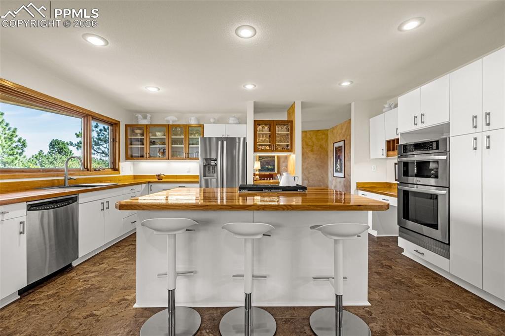 Kitchen with wooden counters, glass insert cabinets, white cabinetry, stainless steel appliances, and recessed lighting