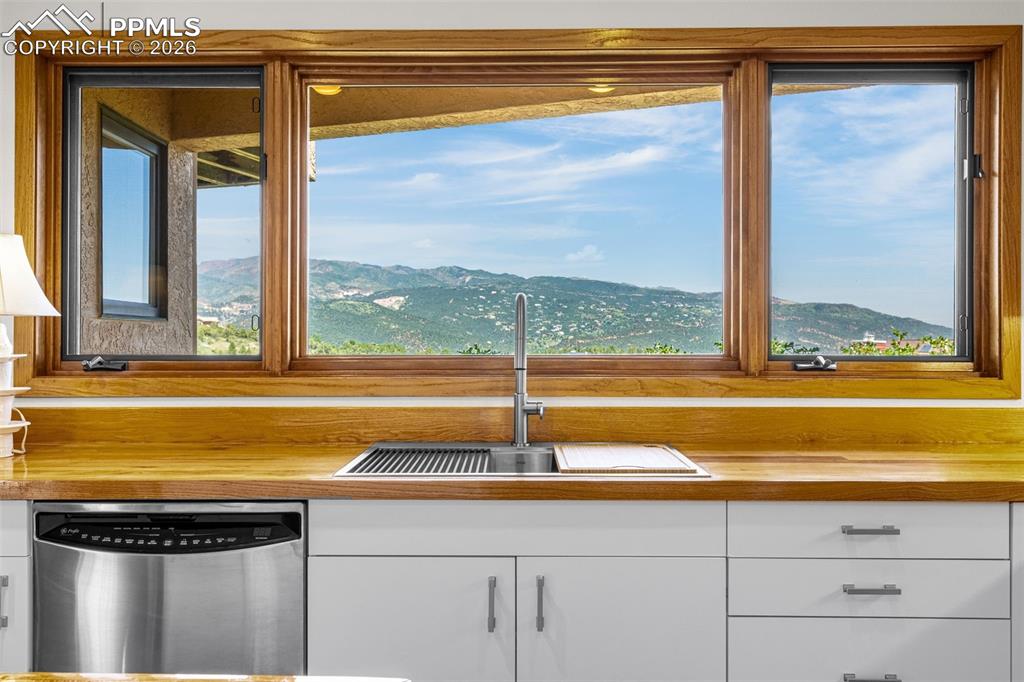 Kitchen with stainless steel dishwasher, a mountain view, and white cabinetry