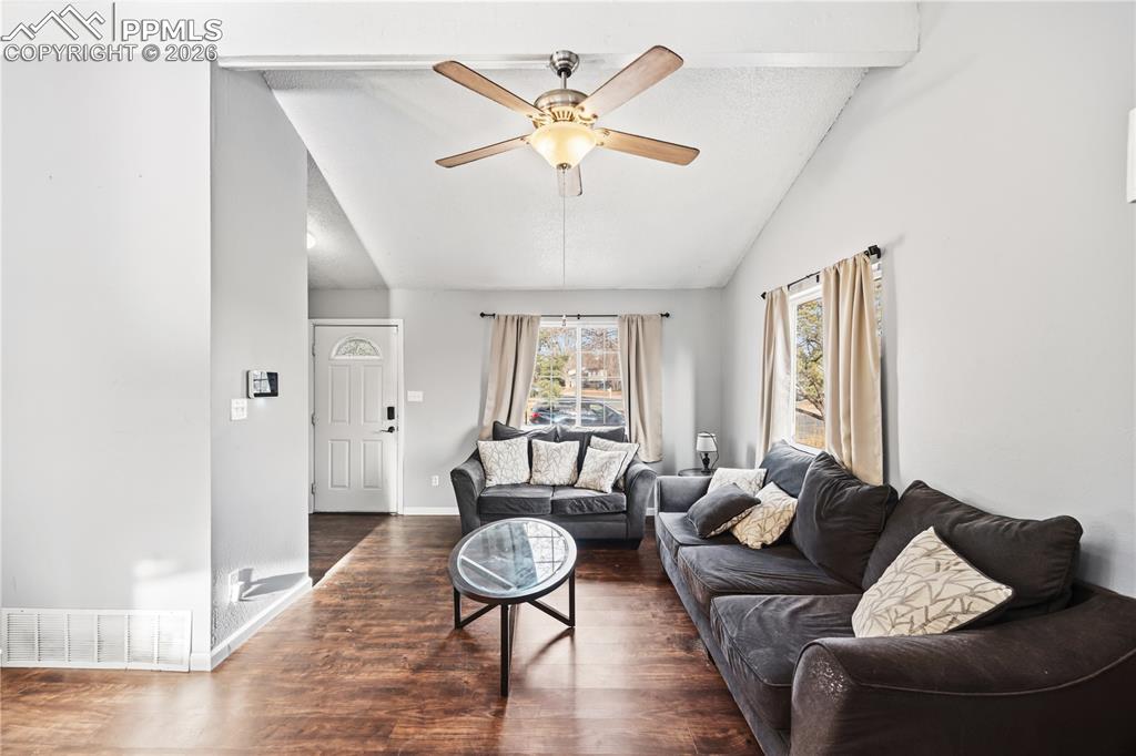 The vaulted living room features LVP floors, a lighted ceiling fan, and views windows of the front yard.