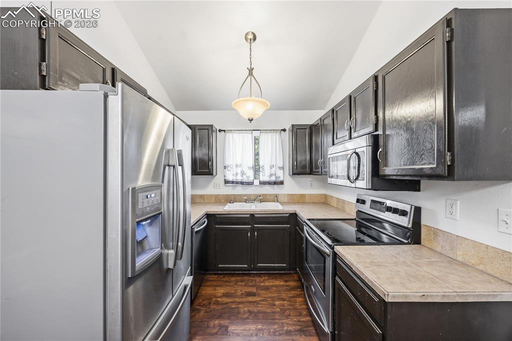 The updated eat-in kitchen showcases espresso cabinetry, tile countertops, a modern light fixture, and stainless steel appliances including a smooth top range oven, dishwasher, built-in microwave, and French-door refrigerator.