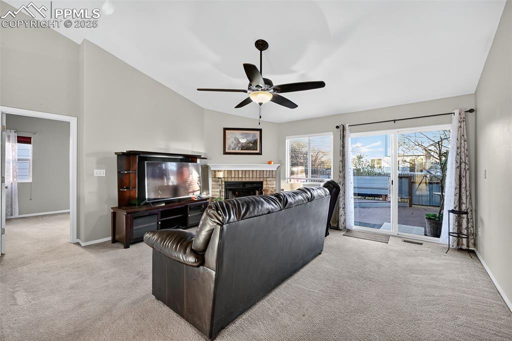 Living area with vaulted ceiling, light carpet, a brick fireplace with Electric insert, and a ceiling fan