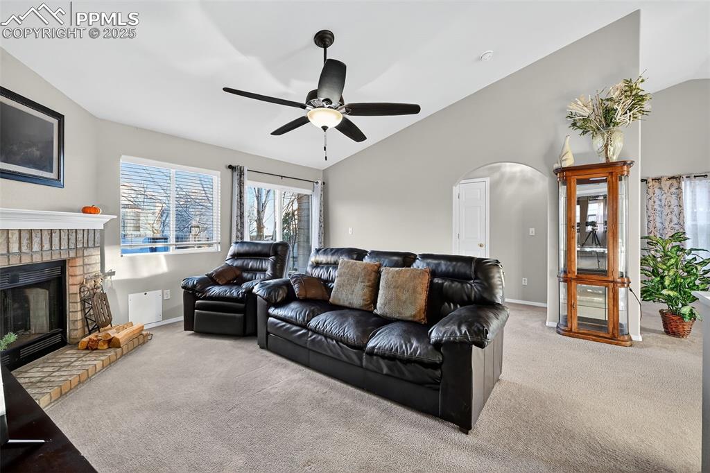 Carpeted living room with lofted ceiling, a brick fireplace, arched walkways, and a ceiling fan...yes there is a Doggie Door!!!  Like the furnishings....They are all available!