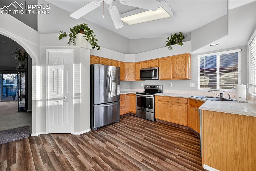 Kitchen with stainless steel appliances, vaulted ceiling, dark wood-type flooring, ceiling fan, and tile counters