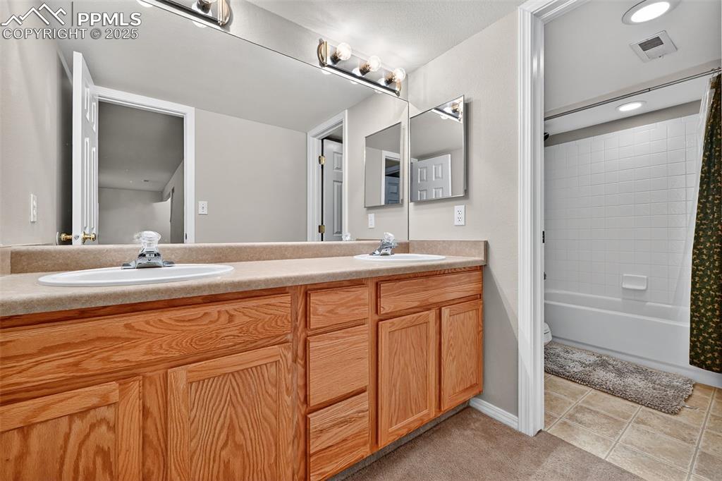 Lower Level Bathroom with double vanity, shower / tub combo with curtain, and light tile patterned floors