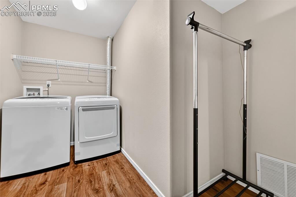 Large Laundry room featuring wood finished floors and washing machine and clothes dryer, room for folding and ironing comes with additional storage cabinet. 